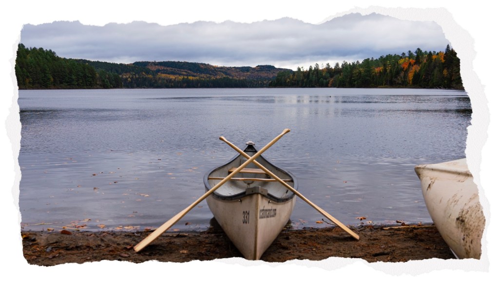Un canoë sur la rive d'un lac entouré de montagnes et de forêts aux couleurs d'automne.