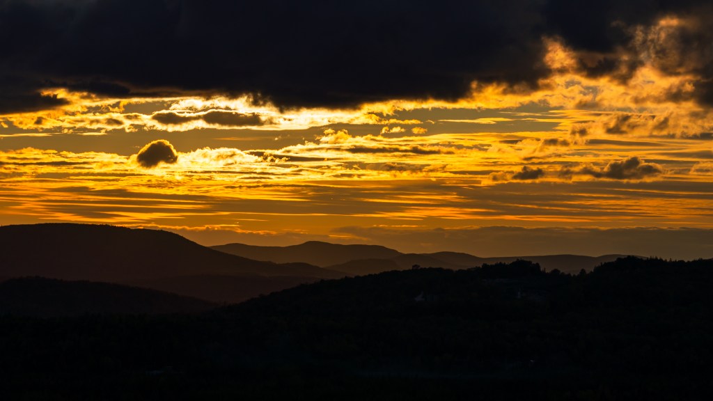 Coucher de soleil sur les montagnes, avec des nuages dorés et des ombres accentuées.