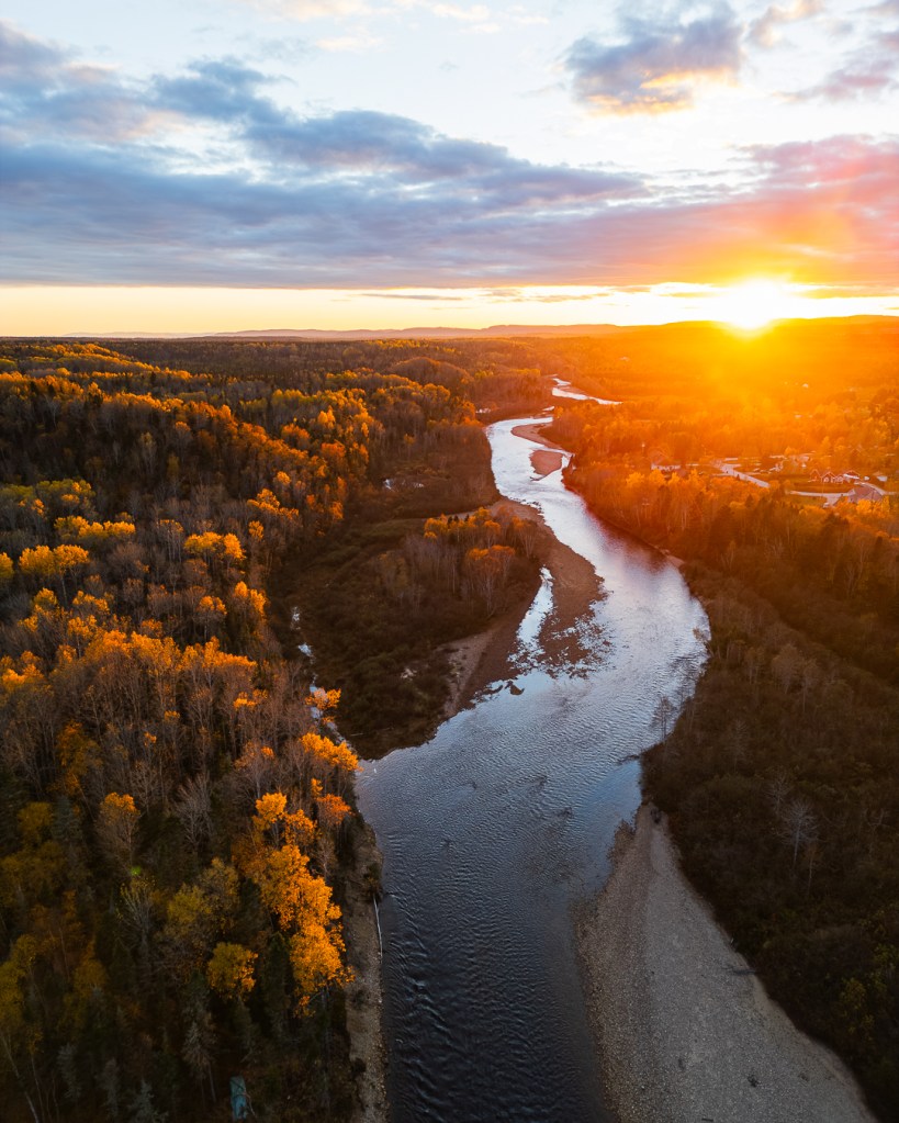 Coucher de soleil sur une rivière entourée de forêts aux couleurs d'automne au Canada.